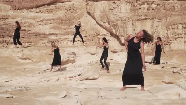 Siyah elbiseli bir grup kadın çöl kanyonunda coşkulu bir dans yapıyor. — Stok video