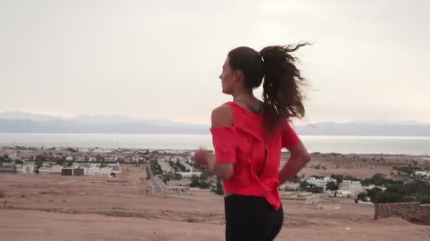 Brunette fille caucasienne jogging le long de la route du désert au bord de la mer — Video