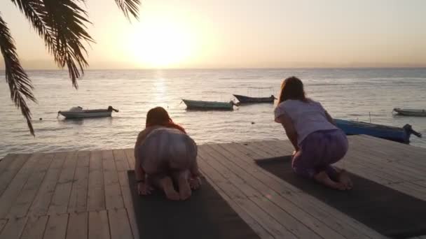 Vista de las mujeres haciendo estiramiento de la práctica de yoga en la playa al atardecer — Vídeos de Stock