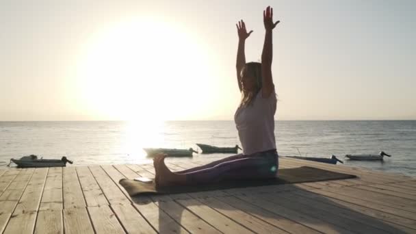 Гибкая женщина, практикующая растяжку йоги на берегу моря под солнцем — стоковое видео