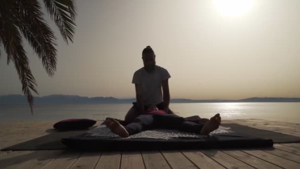 Silhouette of masseur doing thai yoga massage for a woman at sunrise seaside — Stock Video