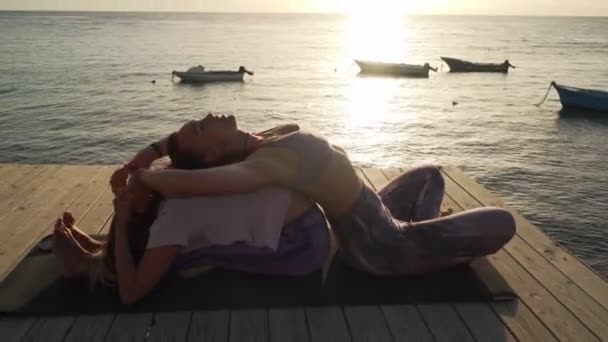 Deux femmes pratiquent assis avant et arrière plie posture de yoga au bord de la mer — Video