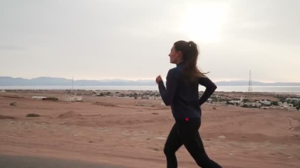 Brunette femme caucasienne jogging le long de la route au bord de la mer — Video