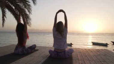 Gün batımında deniz kenarında yoga yapan kadınlar.