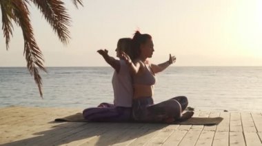 İki kadın, gün batımında deniz kenarında eş yogası için meditasyonu kapatıyorlar.