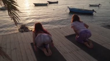 Gün batımında deniz kenarında yoga antrenmanından önce esneme hareketleri yapan kadınlar.