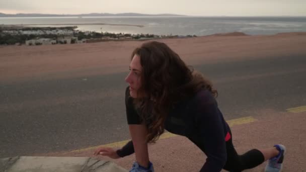 Caucásico chica estiramiento y calentamiento befoe corriendo en carretera por el mar — Vídeo de stock