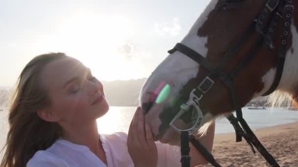 Mladá žena hladí a objímají koně na břehu moře při východu slunce zpomalení — Stock video
