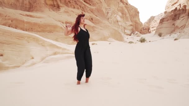 Rossa ragazza in tuta nera pratica danza estatica nel deserto sabbioso — Video Stock