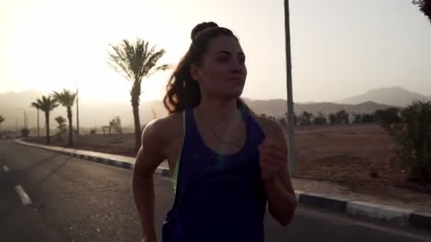 Mladý kavkazský brunetka dívka jogging na tropické dálnici při východu slunce — Stock video