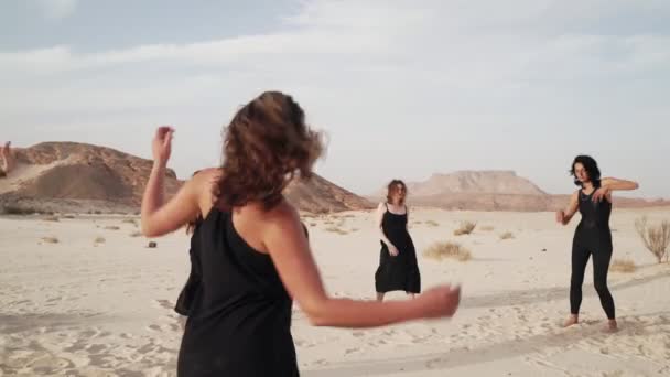 A fekete ruhás nők extázisban táncolnak a sivatagban napkeltekor. — Stock videók