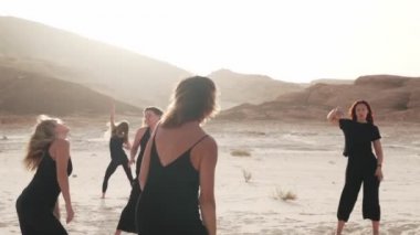 Güneşin doğuşunda çölde, rüzgârlı havada kadınlar coşkulu danslar yaparlar.