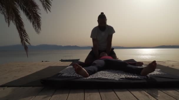 Silhouette del massaggiatore che fa massaggio yoga tailandese per una donna all'alba fuori — Video Stock