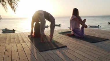 İki kadın gün batımında sahil otelinde yoga yapıyor.