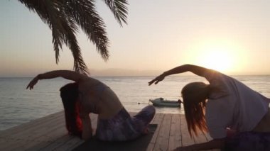 Gün batımında deniz kenarında yoga antrenmanı yapan kadınlar.