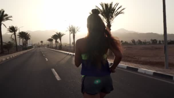 Chica morena joven trotando en la carretera tropical al amanecer — Vídeos de Stock