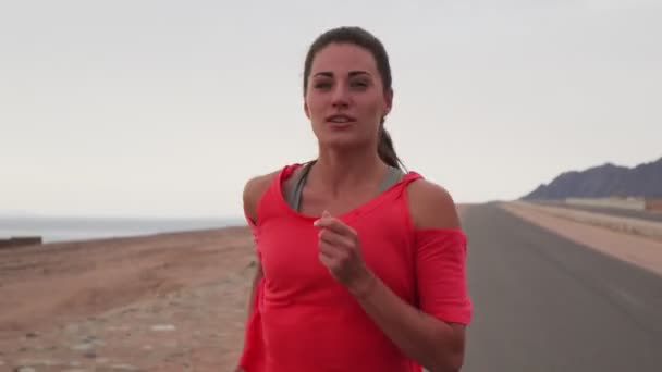 Portré barna kaukázusi lány kocog végig a sivatagi úton a tengerparton — Stock videók