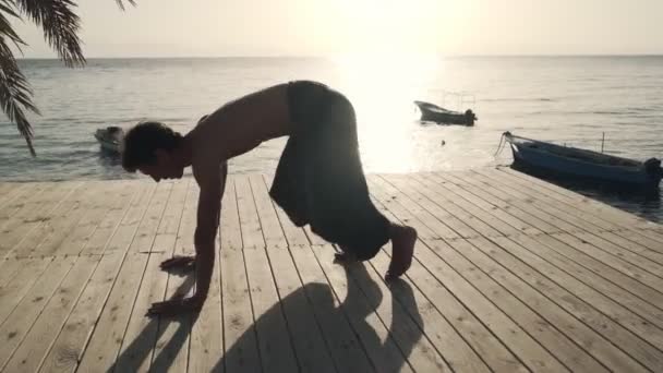 Гнучкий білий чоловік практикує йогу на березі моря в сонячному світлі — стокове відео