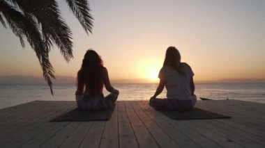 Kadınların silueti gün batımında deniz kenarında esneme egzersizleri yapıyor.