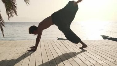 Deniz kenarında güneş ışığında yoga egzersizi yapan esnek genç bir adam.