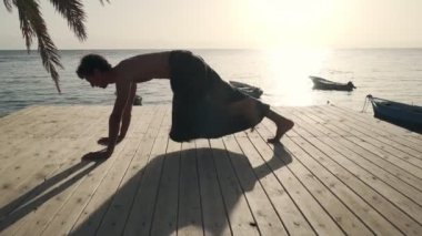 Yakışıklı beyaz adam gün ışığında deniz kıyısında yoga yapıyor.