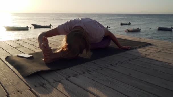 Práctica flexible de la mujer estirando el yoga a la orilla del mar bajo el sol — Vídeos de Stock