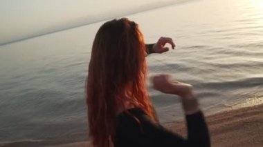 Kızıl saçlı kız deniz kıyısında coşkulu dans alıştırması yapıyor. Dinamik aktif kamera hareketi