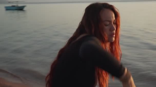 Динамическое движение камеры рыжеволосой девушки практикует экстатический танец на морском побережье — стоковое видео