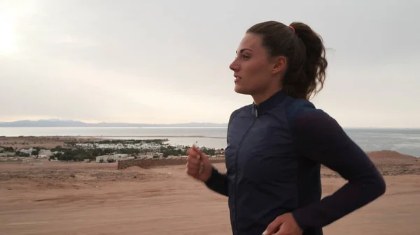 Esmer, beyaz bir kız deniz kıyısında koşu yapıyor.