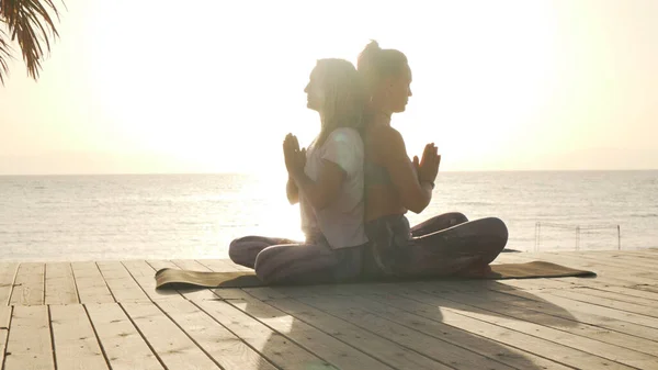 Twee vrouwen oefenen afsluitende meditatie voor partner yoga aan zee bij zonsondergang — Stockfoto