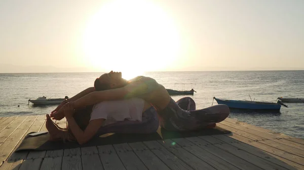 Дві жінки практикують сидіння вперед і назад вигинає пози йоги на морському узбережжі — стокове фото