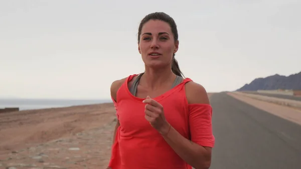 Kumral, beyaz bir kadın deniz kıyısındaki yolda koşuyor.