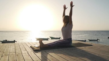Esnek bir kadın, gün ışığında deniz kenarında yoga pratiği yapıyor.