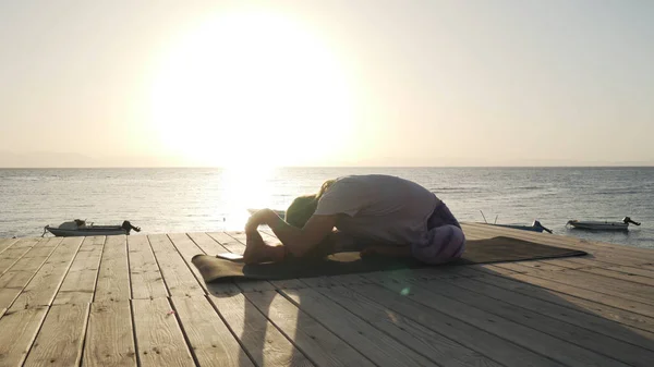 Práctica flexible de la mujer estirando el yoga a la orilla del mar bajo el sol —  Fotos de Stock