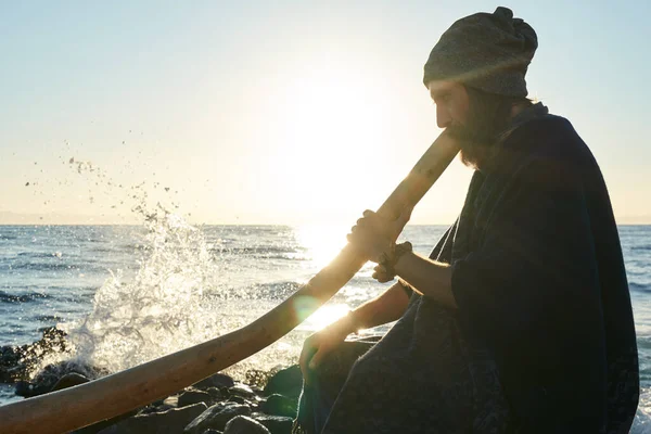 Sakallı adam, didgeridoo Avustralya enstrümanını deniz kıyısında gün ışığında çalıyor..