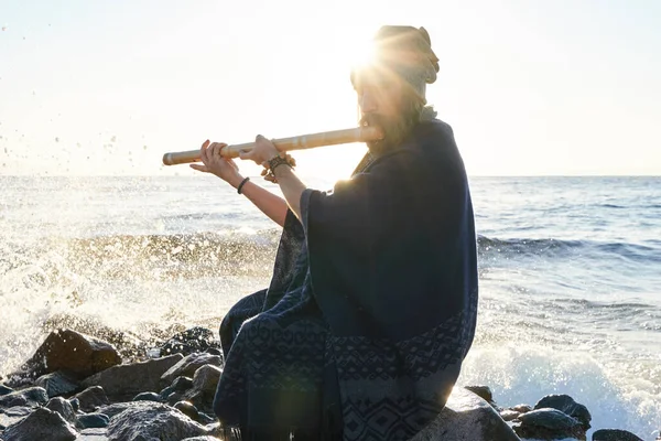 Man bermain di India Bansuri instrumen dalam sinar matahari di pantai laut Stok Foto