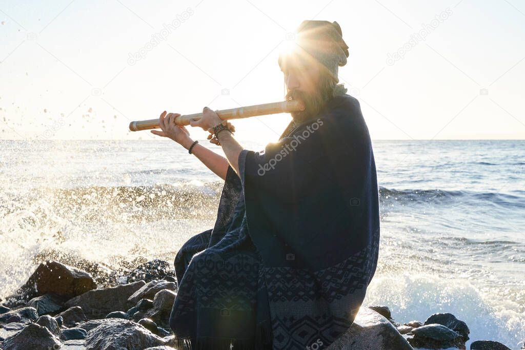 Man playing on Indian Bansuri instrument in sunshine at sea shore