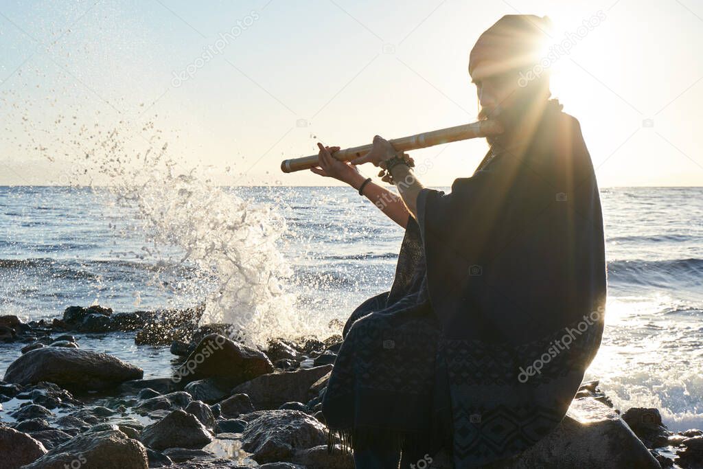 Man playing on Indian Bansuri instrument in sunshine at sea shore