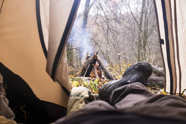 Турист лежить у наметі і дивиться на вогонь у гірському лісі — стокове фото