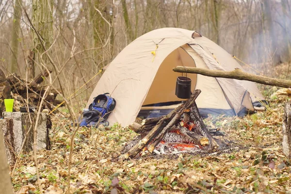 Turist vattenkokare på läger eld med tält på bakgrunden. hand med stick om fire.a — Stockfoto