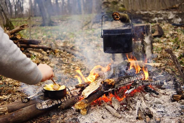 Tourist kettle on camp fire with tent on background. hand with stick about fire.a