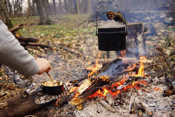 Tourist kettle on camp fire with tent on background. hand with stick about fire.a