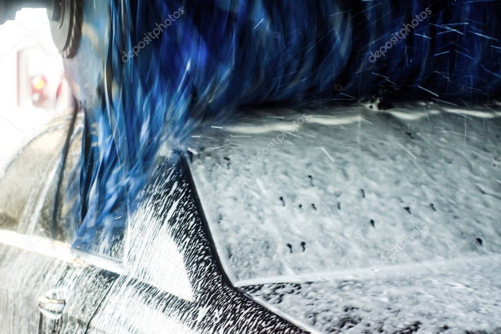Car wash, black car in automatic car wash, rotating red and blue brush. Washing vehicle.