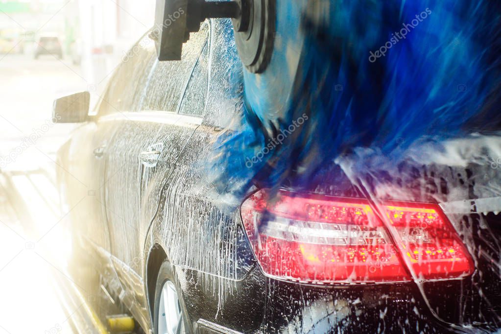 Car wash, black car in automatic car wash, rotating red and blue brush. Washing vehicle.