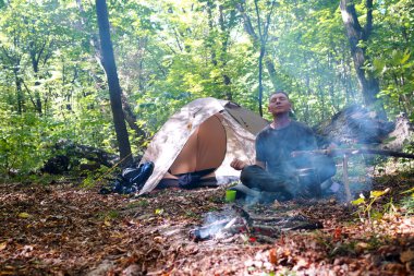 Bir şenlik ateşi ve ormandaki bir turist çadır, çadır turist dinleniyor.