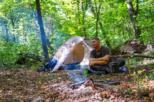 Een vreugdevuur en een toeristische tent in het forest, de toerist is rust in de buurt van de tent. — Stockfoto