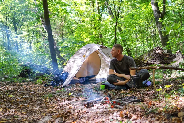 En brasa och en turist tält i skogen, turisten vilar nära tältet. — Stockfoto