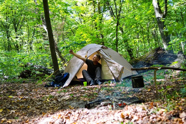 En brasa och en turist tält i skogen, turisten vilar nära tältet. — Stockfoto