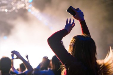 Seyirci bir Müzik Festivali ve sahne yukarıdan aşağı akış ışıklar kaldırdı elleriyle. Yumuşak odak, yüksek ISO, grenli görüntü.