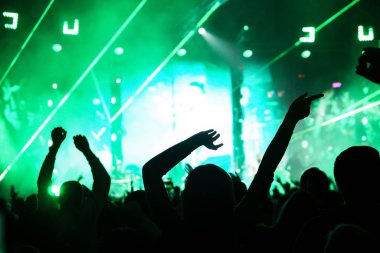 Seyirci bir Müzik Festivali ve sahne yukarıdan aşağı akış ışıklar kaldırdı elleriyle. Yumuşak odak, yüksek ISO, grenli görüntü.